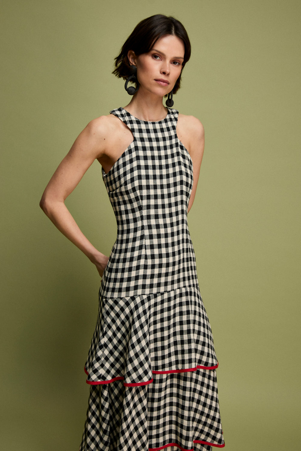 Vestido midi vichy con escote halter y corte en la cintura. La falda está compuesta por volantes viveados en rojo. 